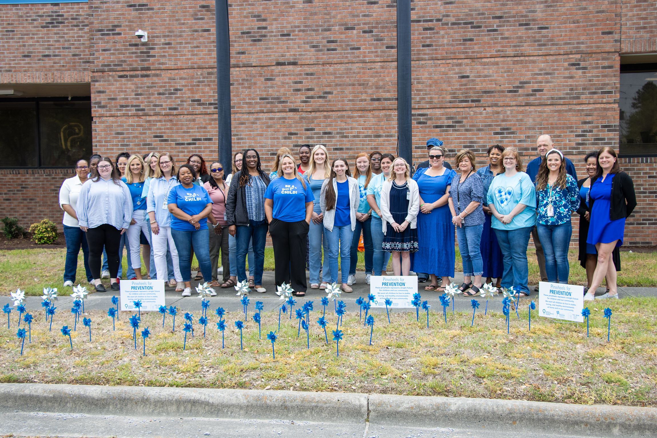 DSS employees and community partners stand behind their pinwheel garden on Friday, April 4, 2025.