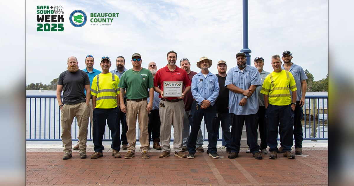 Public Works employees standing with a certificate, with the Washington Waterfront in the background
