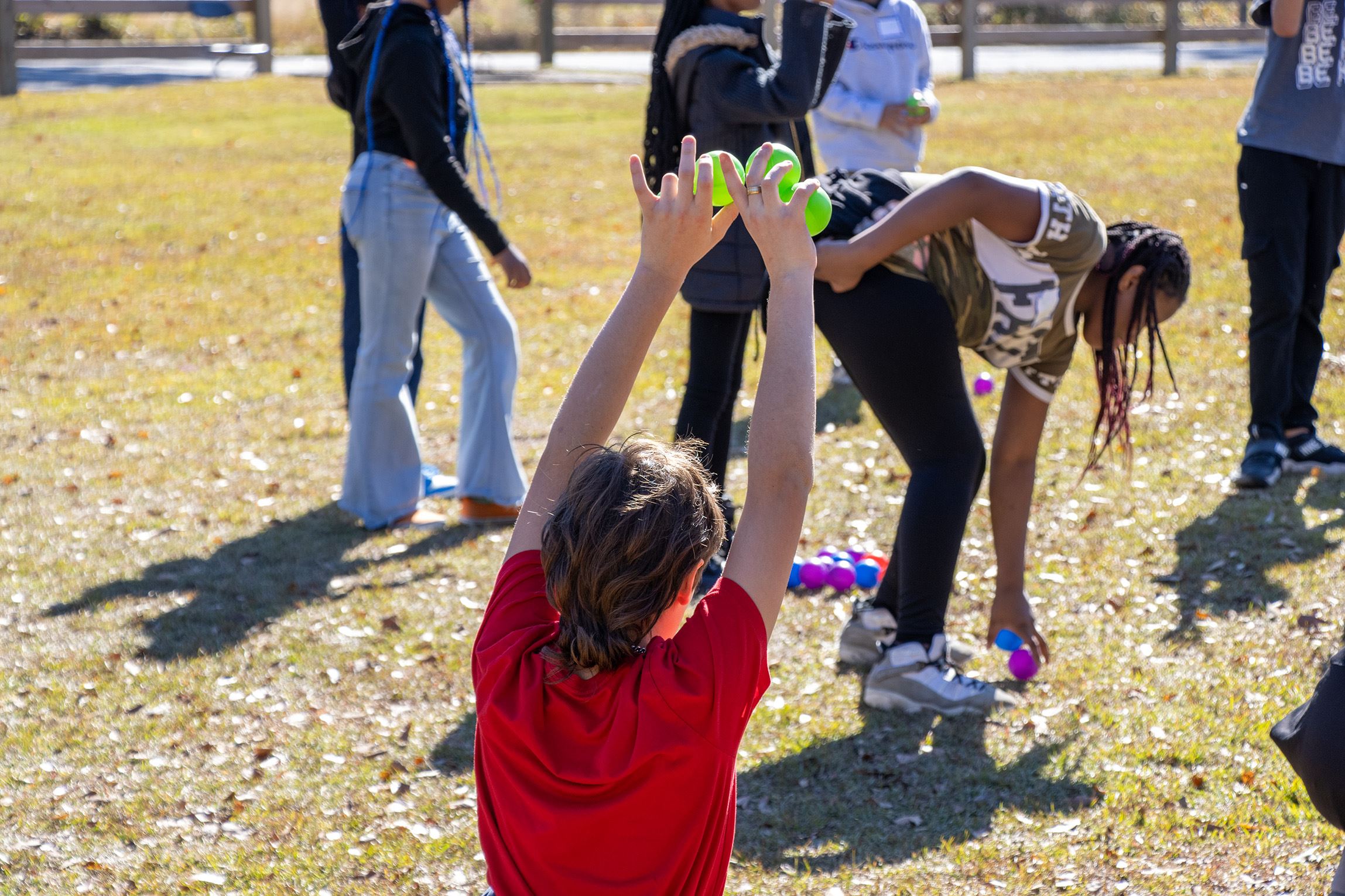 A child, facing away from the camera, holds three green balls above their head during an educational activity