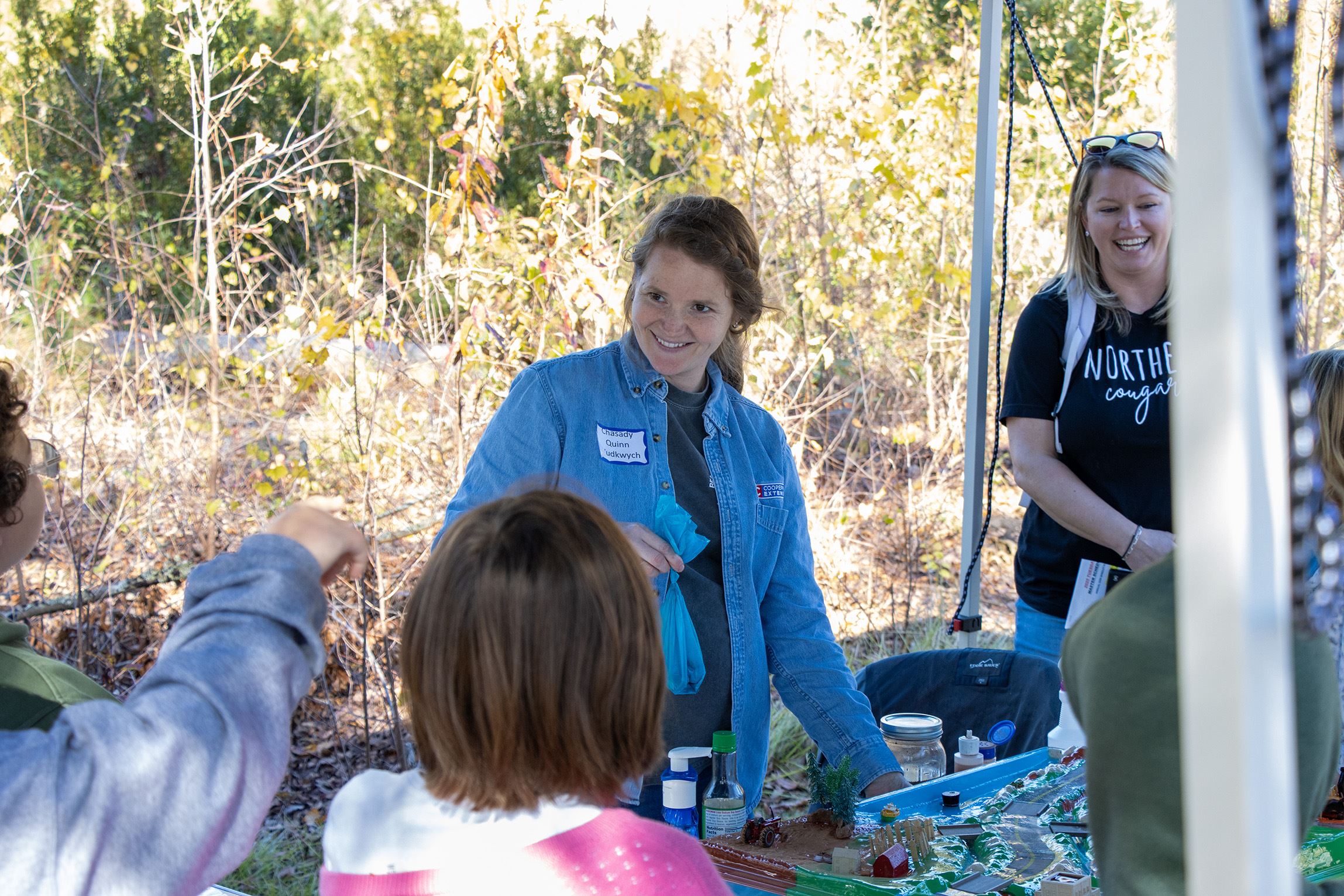 A female instructor smiles while looking over at and acknowledging a student who is responding to a question during an Environmental Field Days activity