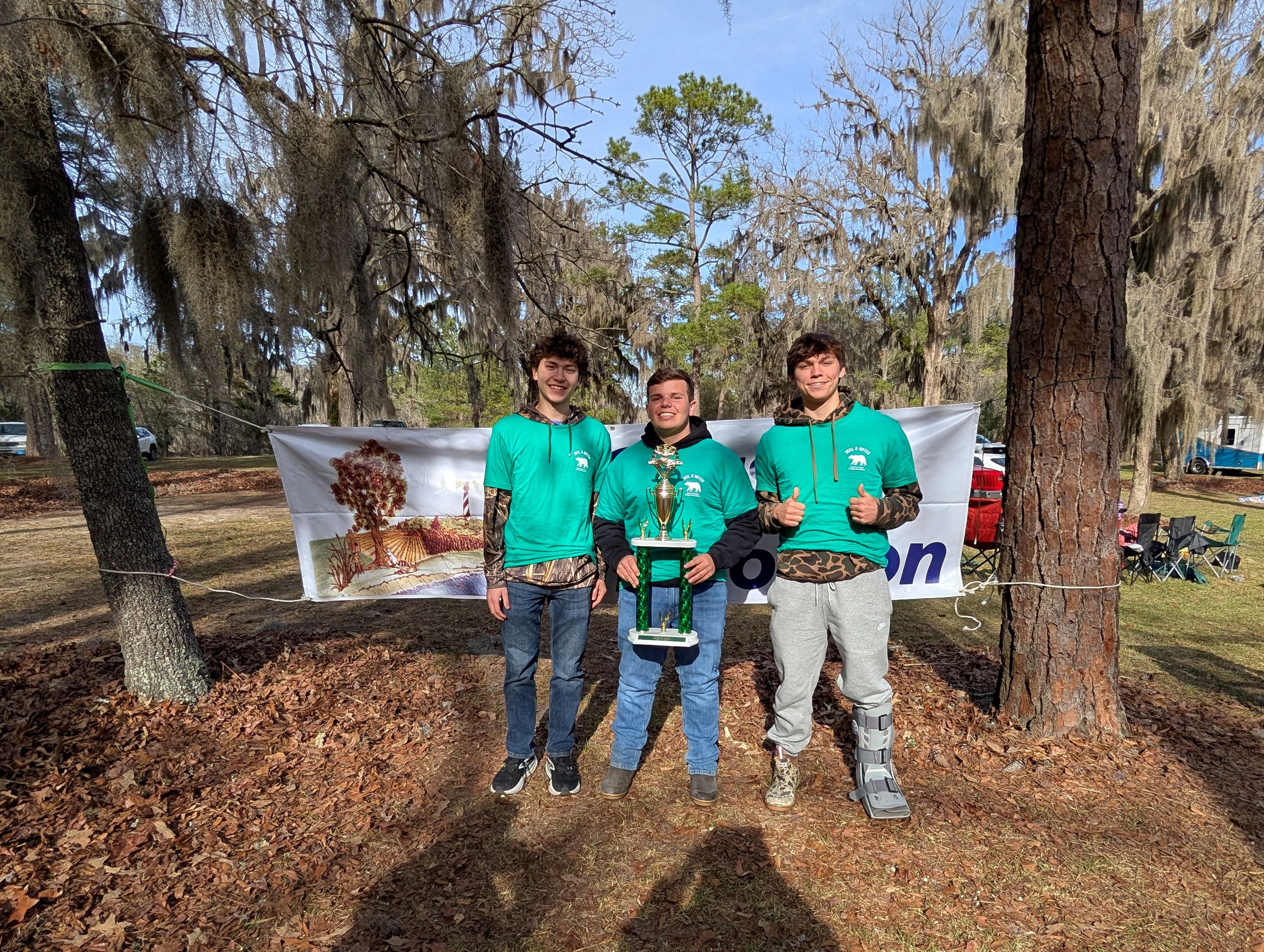 Three male students standing in front of a Coastal Envirothon banner